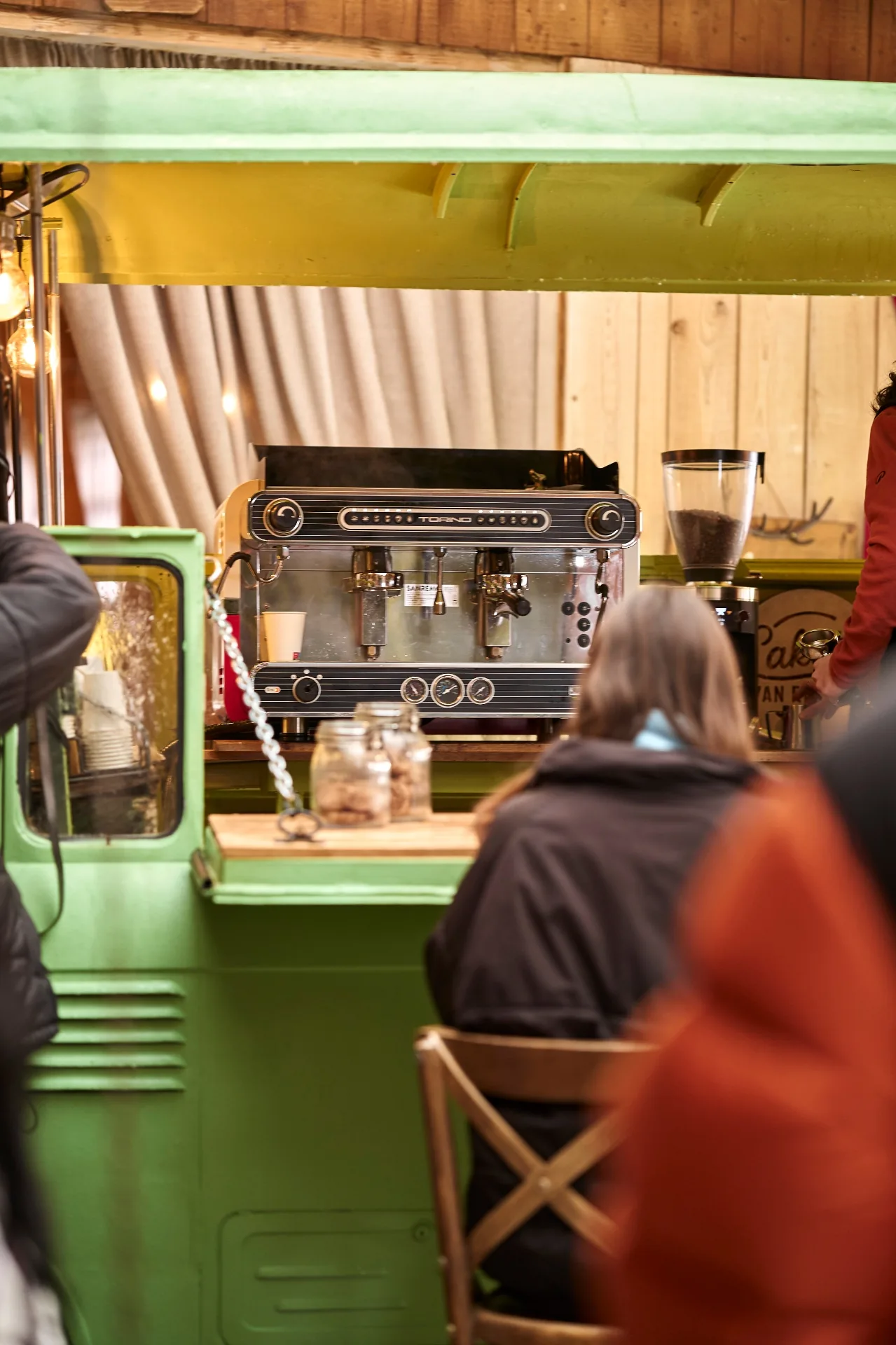 View of the espresso machine across the green van counter with patrons
